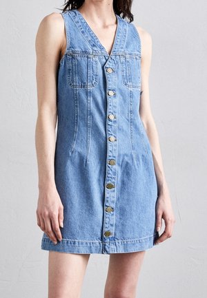 Robe en jean bleu clair avec un design sans manches, un col en V, une fermeture boutonnée devant, deux poches poitrine et une taille ajustée.