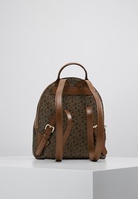 Brown, monogram-patterned backpack with leather straps, zip closure, top handle, and adjustable shoulder straps. Compact, rounded shape.