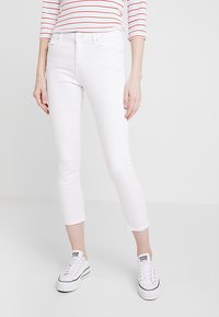 Jeans bianchi cropped con design aderente, realizzati in denim elasticizzato. Presentano orlo sfrangiato e sono abbinati a sneakers bianche. Look semplice e pulito.