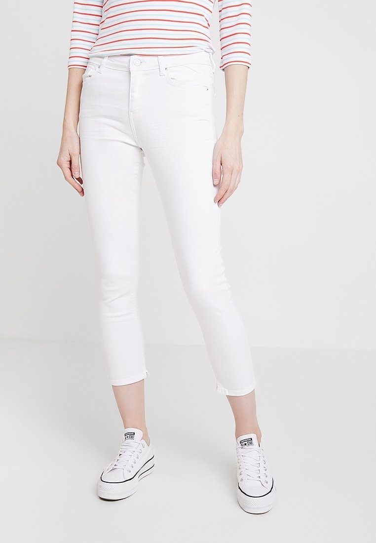 Jeans bianchi cropped con design aderente, realizzati in denim elasticizzato. Presentano orlo sfrangiato e sono abbinati a sneakers bianche. Look semplice e pulito.