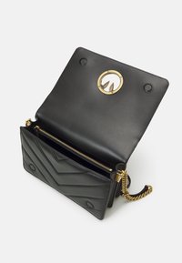 Borsa a mano in pelle nera con cuciture a zigzag, hardware dorato e tracolla a catena. Design aperto che rivela un compartimento con zip e un interno texturizzato.