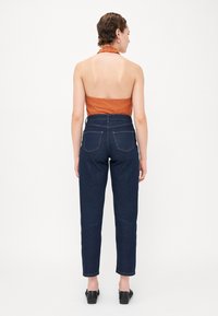 Oranžový halter top s volánkovým výstřihem, v kombinaci s tmavě modrými džíny s vysokým pasem, které mají zadní kapsy a taperovaný střih.