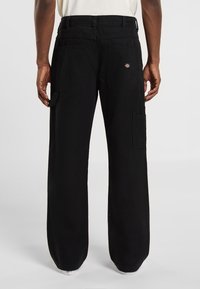 Pantalones cargo negros hechos de tela resistente, que cuentan con dos grandes bolsillos laterales, un corte relajado y una etiqueta de marca visible en la parte trasera.
