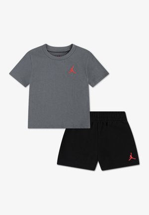 Temno siva majica s kratkimi rokavi in črni kratki hlači z rdečo Jumpman nalepko na prsih in hlačah, položena na ravni beli podlagi.