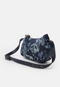 Borsa a spalla in denim con motivo floreale blu, dettagli in oro e una tracolla in pelle scura. Presenta una zip superiore e un dettaglio con logo sulla parte anteriore.