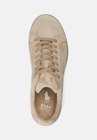 Zapatilla de ante beige con cordones planos, punta redondeada, detalle de logo dorado y plantilla acolchada. Superficie texturizada con acentos de diseño mínimos.