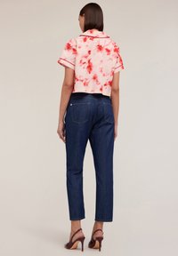 Camicia rosa a maniche corte con motivo tie-dye rosso, abbinata a jeans dritti blu scuro e scarpe con tacco bordeaux.