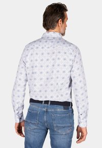 Witte shirt met blauw ruitpatroon, lange mouwen, knoopmanchetten, gecombineerd met blauwe jeans. Zichtbare tailleband met marineblauwe riemaccent.