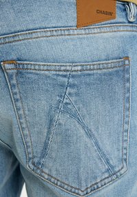 Helle blaue Jeans aus Denim verfügen über ein markantes Design der Gesäßtasche mit einem dreieckigen Stichmuster und einem braunen Lederetikett mit dem Branding "CHASIN'".