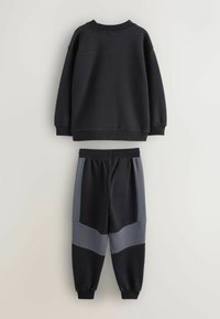 Czarny sweatshirt z okrągłym dekoltem i luźnym krojem wisi nad czarnymi i szarymi joggerami w kolorze blokowym z elastycznym pasem i mankietami.