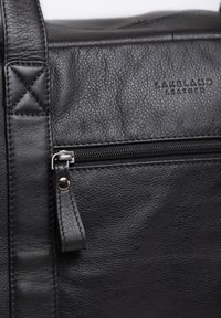 Black leather bag with textured finish, featuring a zip pocket, subtle embossed logo, and sturdy stitching accents. Small metallic hardware detail.