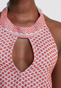 Halterneck top featuring a patterned design in red and white. It has a keyhole cutout and a textured collar. Fabric appears lightweight.