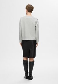 Grijze langesleeve top gecombineerd met een zwarte leren kokerrok en zwarte kniehoge laarzen. De top heeft een ronde halslijn en een ontspannen pasvorm.