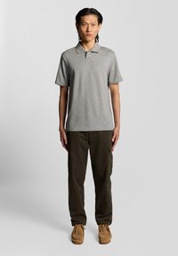 Polo gris à manches courtes avec col, associé à un pantalon cargo olive. Détails notables : plusieurs poches et un design décontracté.