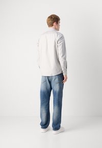 Lys grå langermet skjorte med knappmanchetter, brukt med blå denimjeans. Jeansene har en falmet effekt og en klassisk fem-lommers design.