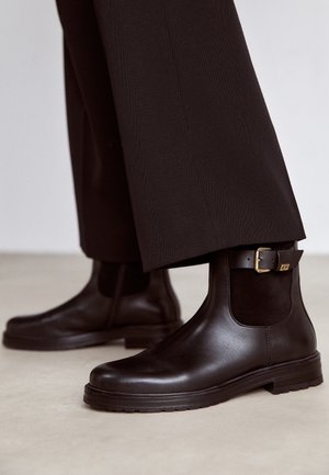 Czarne skórzane botki za kostkę o gładkim wykończeniu, z elastycznym panelem po boku i akcentem w postaci klamry na kostce. Teksturowana podeszwa środkowa.