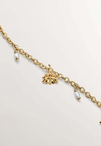 Pulsera de cadena de oro con un charm floral y dos pequeños acentos en forma de bead en azul claro y dorado. Textura suave con un acabado pulido.