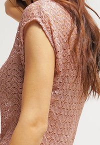 Krajkový top v jemně růžové barvě s vlnitým vzorem, krátkými rukávy a lehkým texturovaným povrchem.