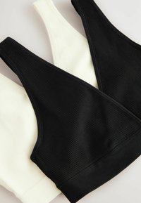 Twee geribbelde bralettes: één zwart, één crème. Beide hebben een ronde halslijn en brede bandjes, met een gladde textuur en geen zichtbare sluitingen.