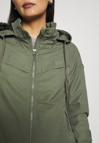 Grøn hættetrøjejakke lavet af letvægtsstof med lynlås foran, elastiske manchetter og sidelommer med snoretræk.