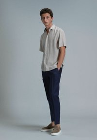 Lichtbeige korte mouwen overhemd met knopen, marineblauwe gestreepte slim-fit broek en beige instappers, tegen een neutrale achtergrond.