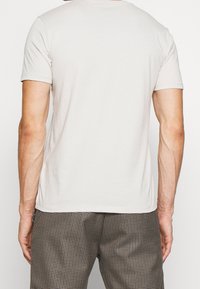 Jasno-beżowy t-shirt z krótkim rękawem, wykonany z miękkiej bawełny, z okrągłym dekoltem i luźnym krojem, o gładkiej fakturze.