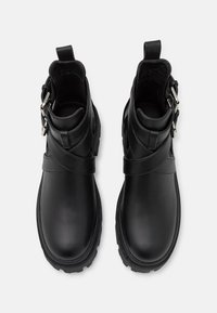 Botas de cuero negro hasta el tobillo con un acabado suave, que presentan una punta redondeada, un tacón bajo y una correa con acentos metálicos.