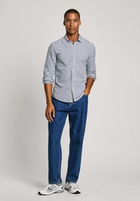Camisa de cuadros en blanco y azul, combinada con jeans de pierna recta oscuros y zapatillas grises. Diseño simple y estructurado.