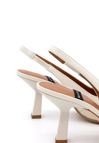 Sandali con tacco alto in pelle bianca, con cinturino slingback, piattaforma curva, soletta beige e dettagli cuciti. Presenta un'etichetta con logo nera.