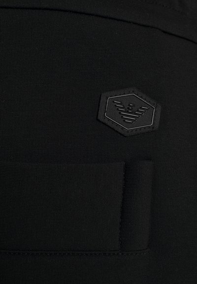 Zwart textiel met een subtiele textuur en een hexagonaal zwart vlak met een verhoogd ontwerp. Inclusief een klein rechthoekig stoffen gedeelte.