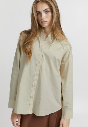 Chemise boutonnée beige à manches longues et à coupe décontractée, avec un col pointu et un ourlet droit. Fabriquée en tissu léger.
