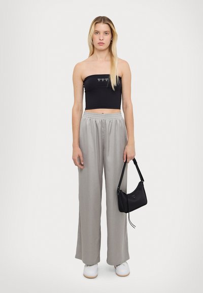 Haut noir sans bretelles avec texte blanc, pantalon large gris clair, baskets blanches et un petit sac à main noir avec une bandoulière.