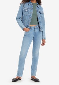 Ljusblå denimjacka med vertikal ribbning, knäppning fram och två bröstfickor, kombinerad med raka ljusblå jeans och svarta mule-skor.