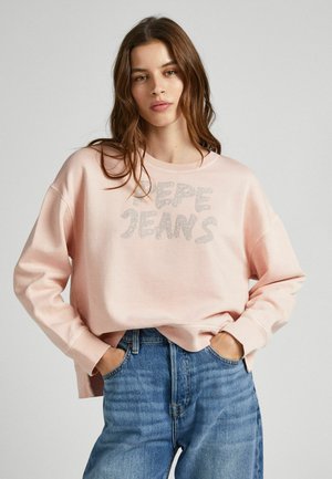 Felpa rosa chiaro con collo rotondo e vestibilità oversize, con la scritta "PEPE JEANS" in lettering argentato testurizzato. Abbinata a jeans in denim blu.