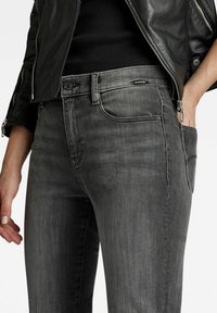 Grey denim jeans with a slim fit, featuring a front pocket, subtle fading, and a G-Star logo on the waistband. Smooth texture and classic design.