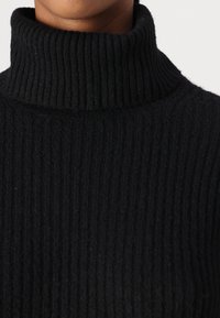 Črni rebrasti pulover s turtleneck ovratnikom in strukturiranim pletenjem, zasnovan za tesno prileganje.