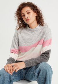 Lysegrå og pink stribet sweater med ribbet krave og lange ærmer. Teksturen ser blød ud, parret med lyseblå jeans.