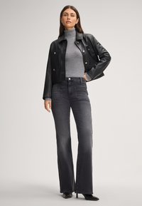 Giacca cropped in pelle nera con bottoni argentati, dolcevita grigia e jeans svasati grigio scuro. Stivaletti con tacco a spillo aggiungono altezza.