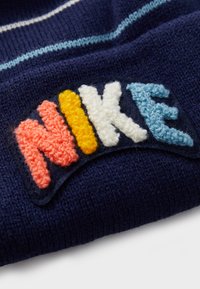 Mornarsko pleteno blago s vodoravnimi črtami; vsebuje teksturiran, večbarven vezen "NIKE" logotip v svetlo rožnati, rumeni, beli in svetlo modri barvi.