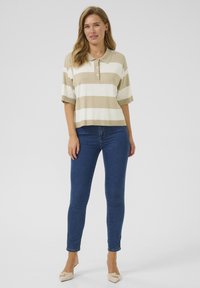 Beige och vit randig polo med krage, korta ärmar och tre knappar, tillsammans med blå slim fit-jeans och ljusa skor.