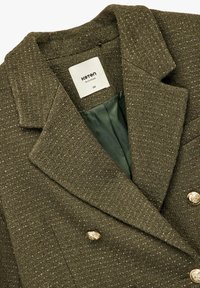 Dubbelzijdige groene blazer gemaakt van gestructureerde stof met gouden knopen en een satijnen binnenvoering. Etiket vermeldt "Koton, maat 38."