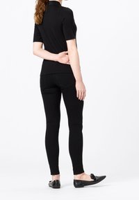 Mustat lyhythihaiset yläosat yhdistettynä istuviin mustiin housuihin, joissa on siisti muotoilu ja sileä pinta. Kengät ovat mustat, matalat, rusettiyksityiskohdalla.