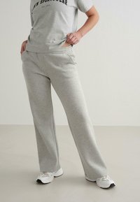 Lys grå sweatpants i bomuldsblanding med en afslappet pasform, der har sidelommer og en glat tekstur, kombineret med en grå grafisk t-shirt og hvide sneakers.