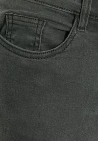 Harmaan denimi, jossa on lähikuva etutaskusta, jossa on ommellut reunat ja sileä pinta, esitellen minimalistischia muotoiluyksityiskohtia.