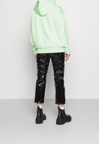 Sudadera verde menta con capucha ajustable, combinada con pantalones cortos de cuero negro brillante. Se llevan botas negras de plataforma con suela gruesa.