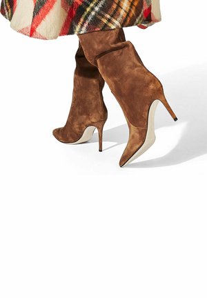 Bordeaux gekleurde suède kniehoge stiletto laarzen met spitse neuzen en een slanke hak, gecombineerd met een veelkleurige geruite rok in rode en gele tinten.
