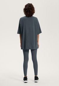 Överdimensionerad mörkgrå t-shirt ihop med åtsittande mörkgrå leggings med kontrastsömmar, kompletterat med svarta träningsskor.