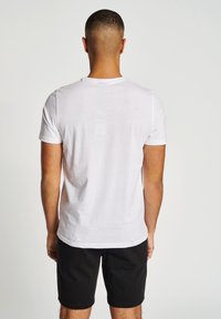 Hvid kortærmet t-shirt lavet af blødt stof, vist fra ryggen med rund hals, parret med sorte shorts.