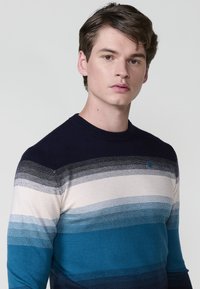 Suéter de rayas para hombre en azul, marino y crema. Textura de punto con líneas horizontales en degradado y cuello redondo. Presenta un pequeño logo en el pecho.