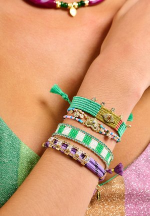Bracelets colorés avec des motifs tissés et des perles dans des nuances de vert, violet et or, ornés de pompons et de breloques décoratives.